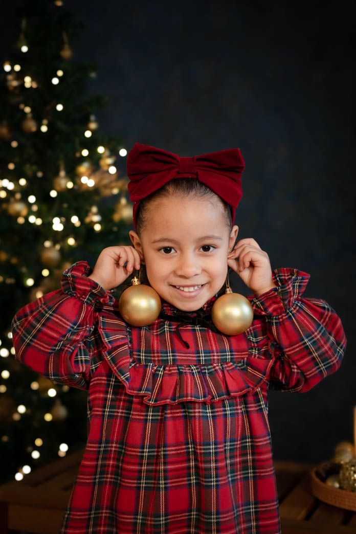niña con vestido jugando con decoración de arbolito de navidad en set de sesiones de aleiram fotografia